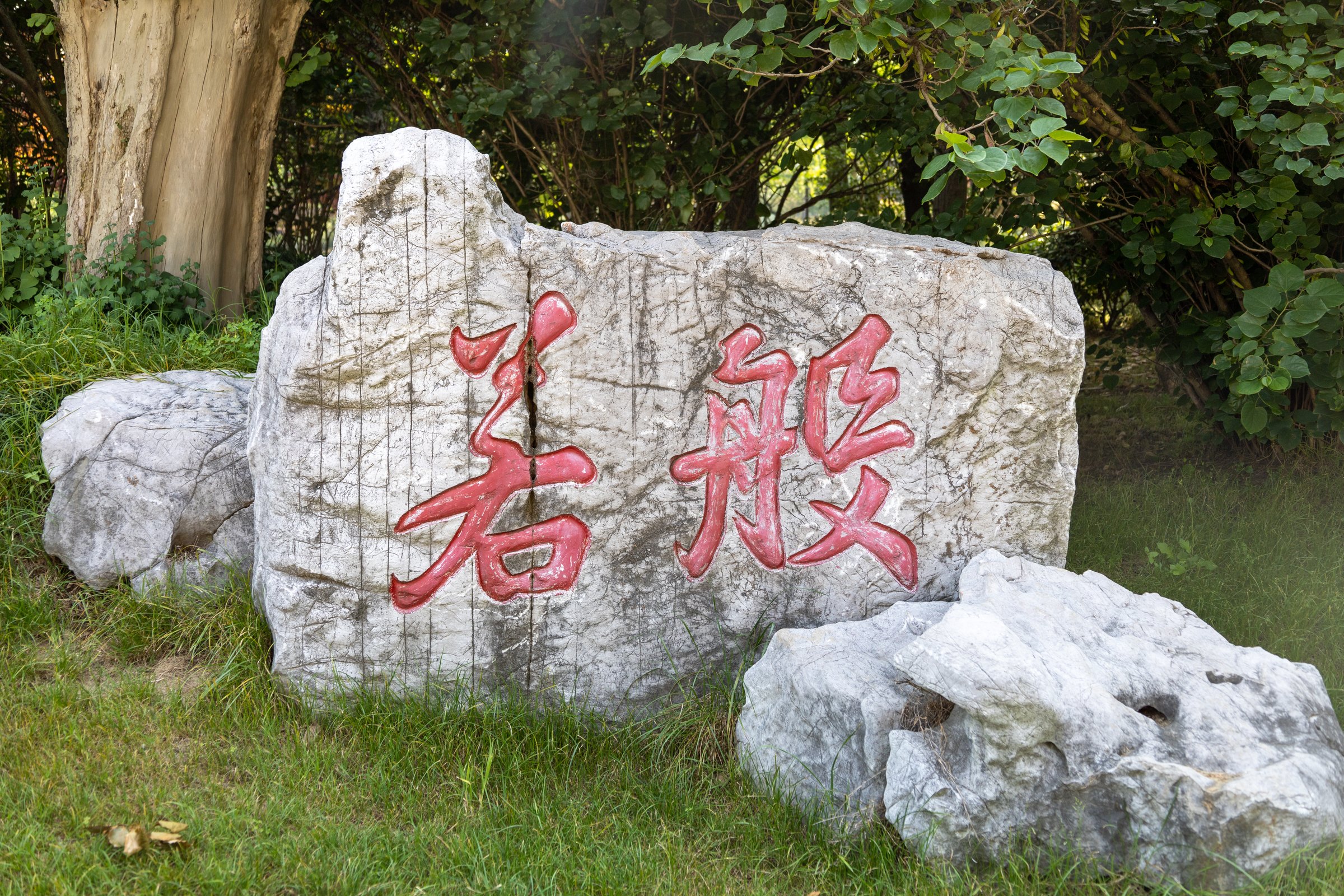 草地边的浅灰岩石上刻有两个红色大字,周围是小石块和树丛。