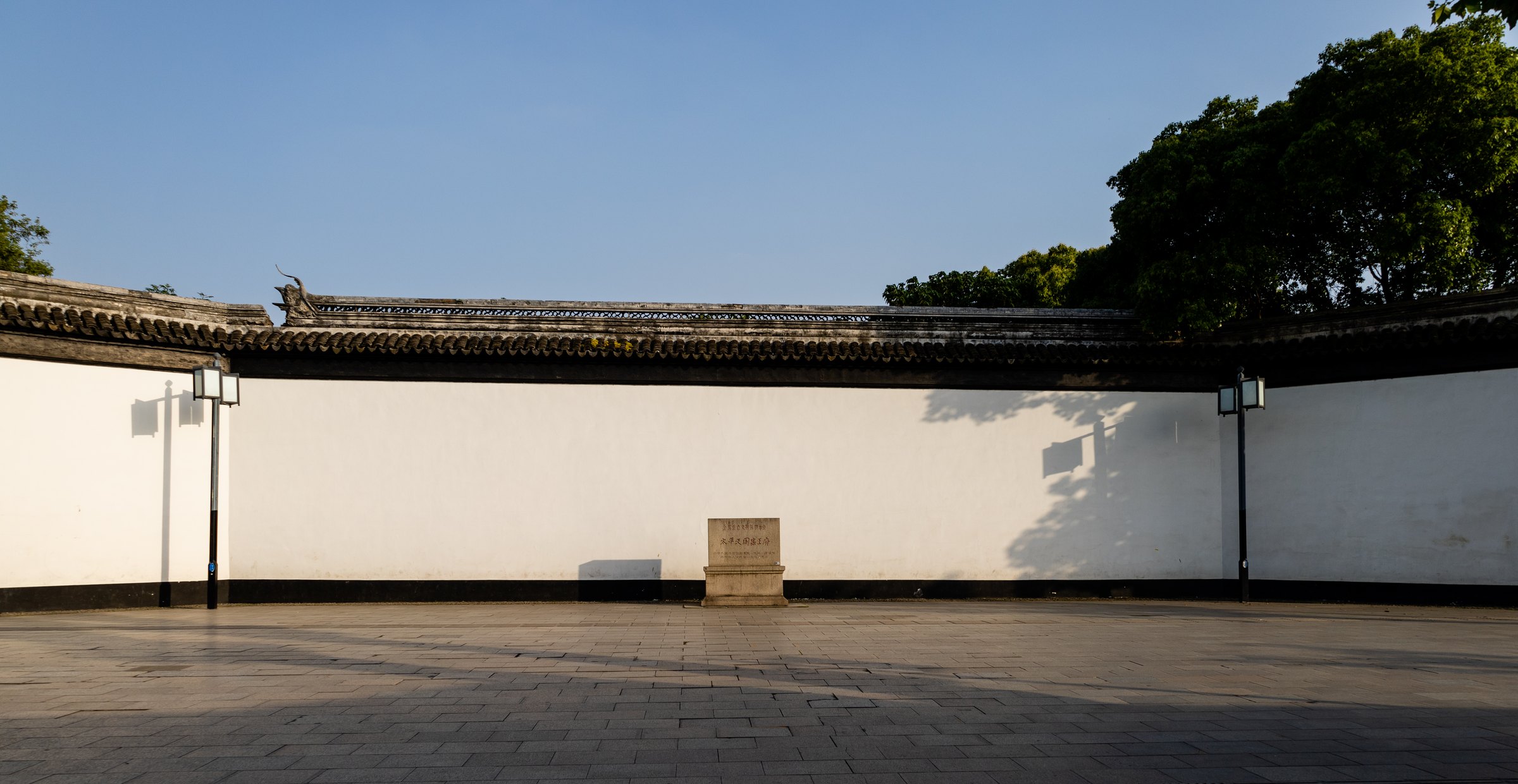 宽阔石铺空地尽头是一面长白墙,灰瓦沿墙顶延伸,中央立着小石牌。