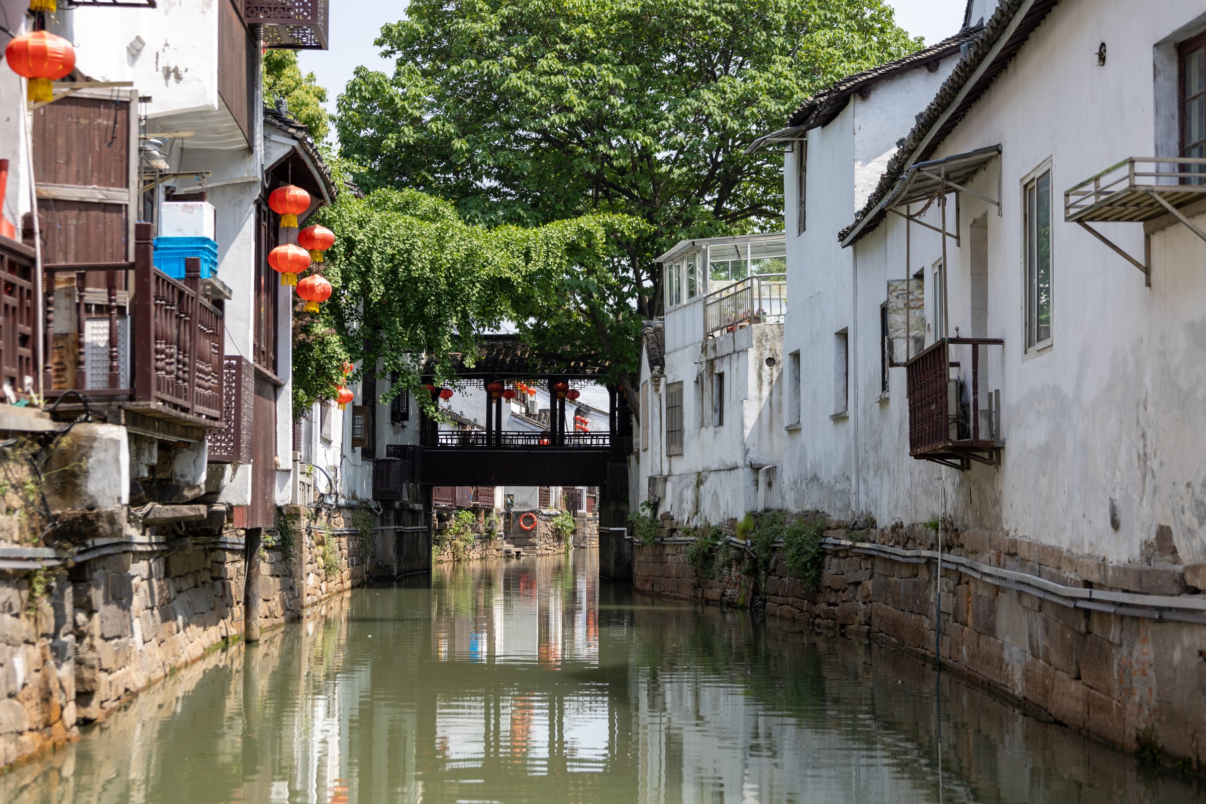 狭窄水道两边是白墙石基建筑,前方横跨一段深色廊桥。