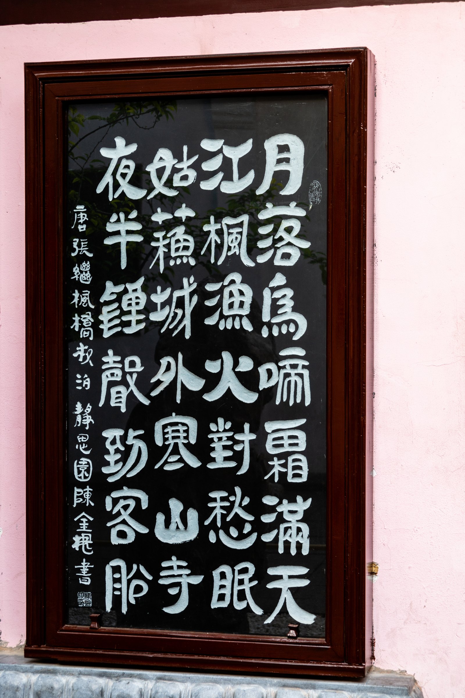深色木框中的黑底白字书法挂在浅色墙面上,正文竖排成多列。
