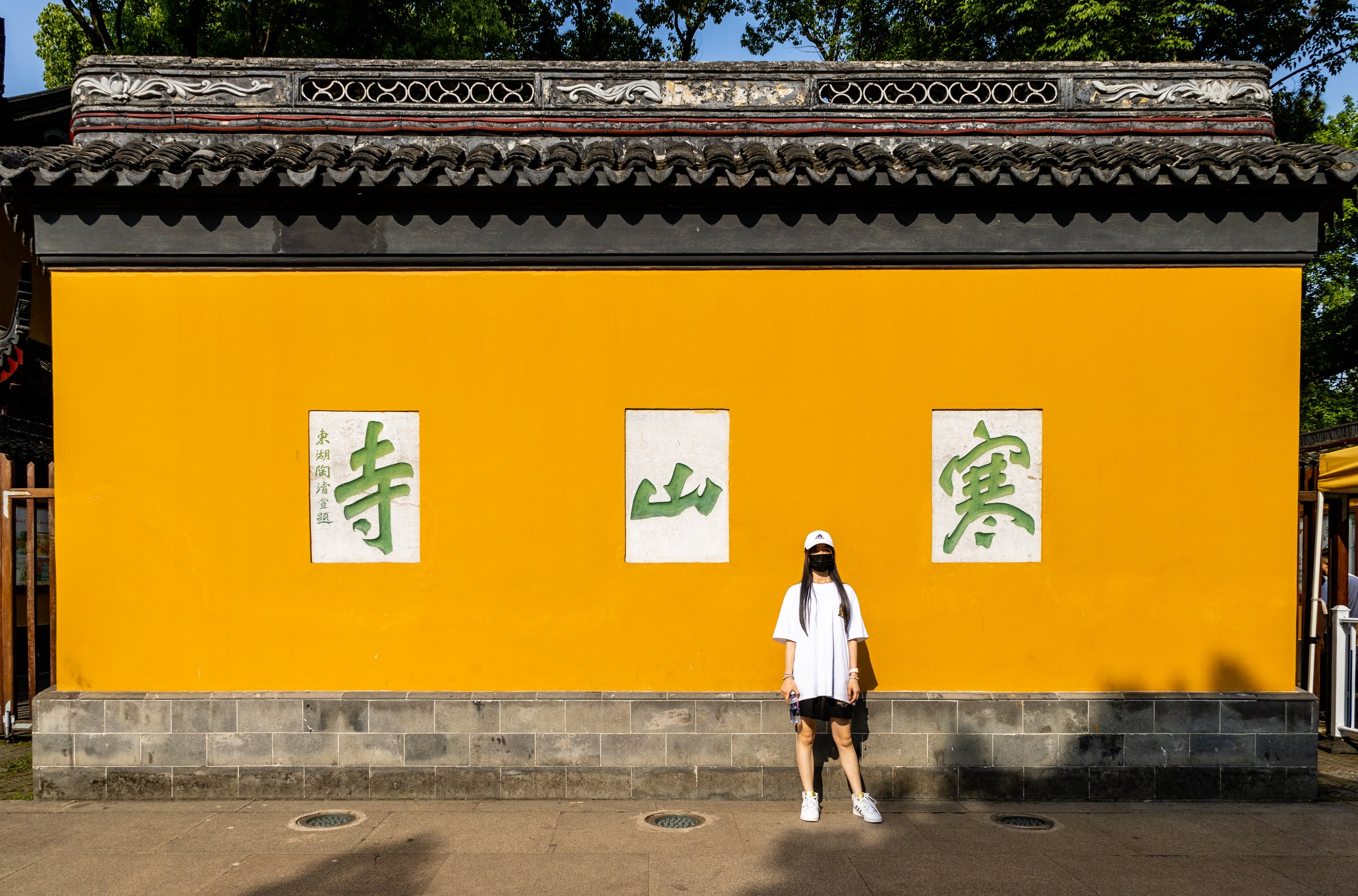 一名戴白帽和黑色口罩、穿白色上衣的人站在黄墙前,墙上有绿色大字。